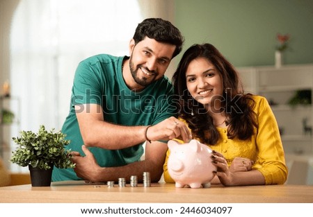 Indian asian young couple and saving concept putting coins in piggy bank at home