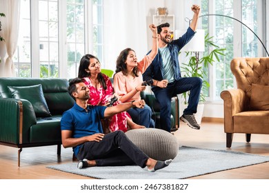 Indian asian young friend couple playing video games with joystick remote together while sitting on sofa - Powered by Shutterstock