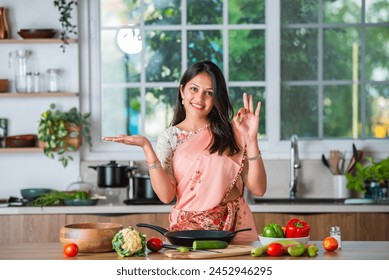 Indian asian young woman pointing, shocasing or promoting utensils, pot, spatula, empty plate, ok sign - Powered by Shutterstock