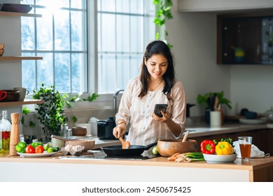 Indian asian young woman using smartphone in kitchen while cooking - Powered by Shutterstock