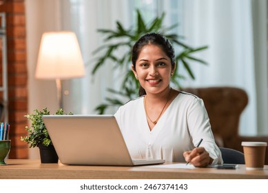 Indian asian young working professional female working on laptop at home wears smart formals