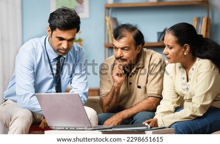 Indian banker explaining about insurance policy or savings scheme on laptop to senior couple while sitting on sofa at home - concept of banking support, and bonding