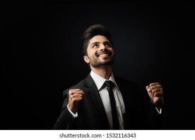 Indian Bearded Male businessman celebrating success with thumbs up or raising fist while standing isolated over black background