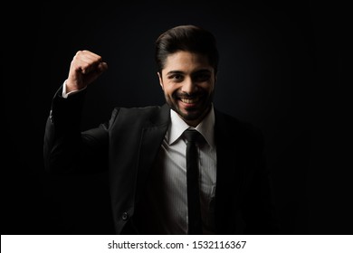 Indian Bearded Male businessman celebrating success with thumbs up or raising fist while standing isolated over black background