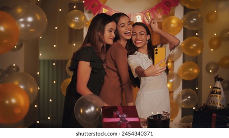 Indian beautiful young adult female friends standing use mobile taking selfie enjoy indoor decor home. Modern teen Influence girls hold phone look cam make content video shoot celebrate birthday house - Powered by Shutterstock