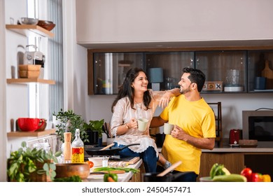 Indian beautiful young couple having coffee in kitchen while cooking food - Powered by Shutterstock