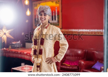 Indian boy dressed in Bollywood clothes and turban with hands on hips looking at camera and smiling