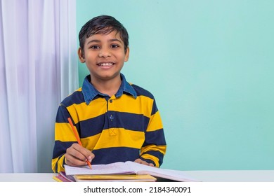 Indian Boy Student Doing Study At Home, He Is Writing On Notebook And Doing His Homework