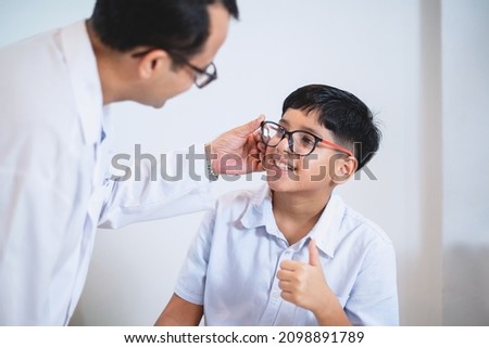 Indian boy try eyeglass frames and thumb up  it's perfect for him, optometrist or optometrist  helps to get new glasses for boy