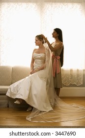 Indian Bridesmaid Placing Veil On Caucasian Bride.