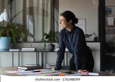 Indian business coach accomplish preparation for seminar feel satisfied looking in distance. Motivated enthusiastic employee work on project research statistics take break standing in office boardroom