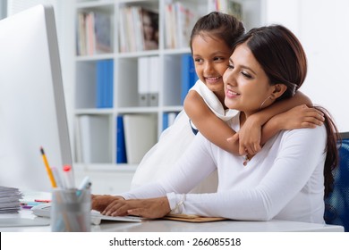 Indian business lady working on computer while her daughter hugging her