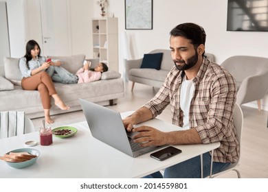 Indian Business Man Father Distance Worker Remote Working Online From Home Office With Family. Busy Parent Dad Using Laptop Computer Sitting At Table In Homeoffice Having Virtual Meeting On Freelance.