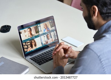 Indian Business Man Having Virtual Team Meeting On Video Conference Call Using Laptop Work From Home Office Talking To Diverse People Group In Remote Teamwork Online Distance Chat. Over Shoulder View