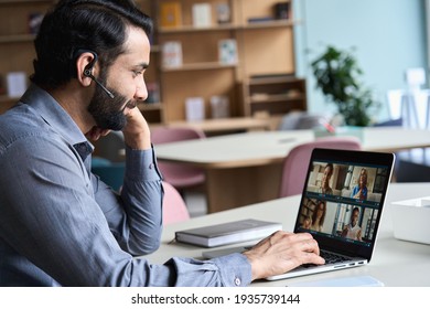 Indian Business Man Wearing Headset Having Virtual Team Meeting On Video Conference Call, Using Laptop Work From Home Office Talking To Diverse People Group In Remote Team Zoom Online Distance Chat.