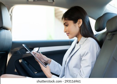 Indian Business Woman Using Tablet Pc In Backseat Of Car 