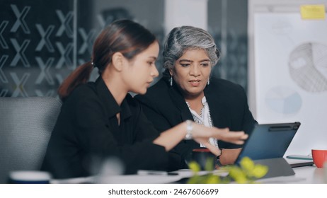 Indian business women sitting on chair using tablet look screen discuss share new project plan ideas job office place. Young adult colleagues old elder female doing work task together indoor workplace - Powered by Shutterstock