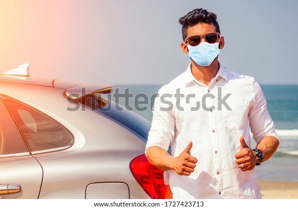 Indian businessman in car outdoors on sea\
beach summer good day.a man in a white shirt and mask rejoicing\
buying a new car enjoying a vacation by the\
ocean
