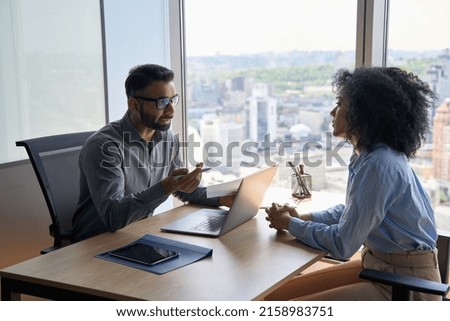 Indian businessman ceo hr director having interview holding paper cv hiring for job female African American applicant sitting in contemporary office. Human resources recruitment concept.