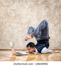 Indian Businessman Doing Yoga And Looking At Laptop In The Office At Brown Textured Background