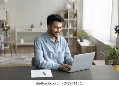 Indian businessman, freelance worker sit at desk with computer, working on-line from home, using laptop, typing message, solve business by e-mailing, correspond to client, do task. Workflow using tech - Powered by Shutterstock