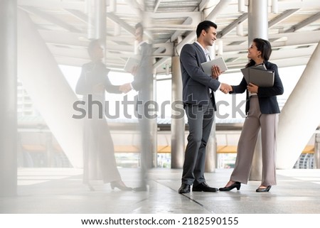 Indian businessman greeting and making handshake with a businesswoman outdoors in city walkway