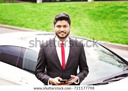 Indian businessman with smartphone standing near car outdoors