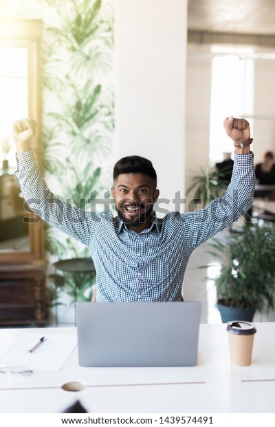 indian businessman and success or victory sign\
with stretched hands while sitting and looking at computer screen\
in the office