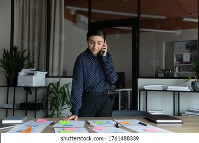 Indian Businesswoman Project Leader Prepare Presentation For Company Investors Use Colorful Post-it Notes Printed Graphs Charts Financial Data Overview And Forecast Talk By Phone Standing At Boardroom