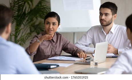 Indian businesswoman speaking, sharing ideas with diverse colleagues at corporate meeting, business partners discussing strategy, project statistics or financial report, sitting at table in boardroom