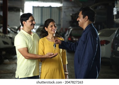 Indian car mechanic delivering the car keys to the happy customers. Portraying customer satisfaction to the whole scene the cheerful car specialist is returning the keys after repairing their vehicle. - Powered by Shutterstock