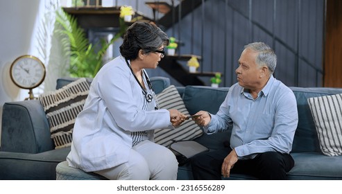 Indian caring female pharmacist doctor visit senior patient house sitting on chair gives medicine tablet and explaining about prescription help prescribing drug at medical healthcare consultation  - Powered by Shutterstock