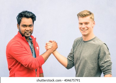 Indian and caucasian men shaking hands in a modern handshake to show each other friendship and respect - Best friends having arm wrestling against racism on blue wall - Soft desaturated filtered look