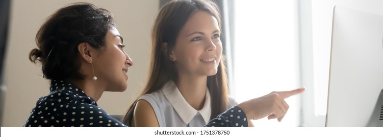 Indian And Caucasian Multi Ethnic Girls Colleagues Working Together Using Computer, Mentor Point On Device Screen Explain Corporate Program To Intern. Horizontal Photo Banner For Website Header Design