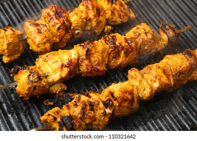 Indian chicken tikka kebabs, marinated in spices and yogurt, cooking on griddle plate. Shallow DoF, focus on centre.