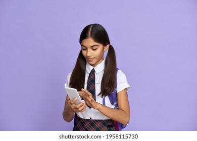 Indian Child Wearing School Uniform With Backpack Holding Cellphone Watching Streaming Online Video. Arab Teenage Girl With Ponytails Using Mobile App For Learning Class. Portrait Isolated On Violet.