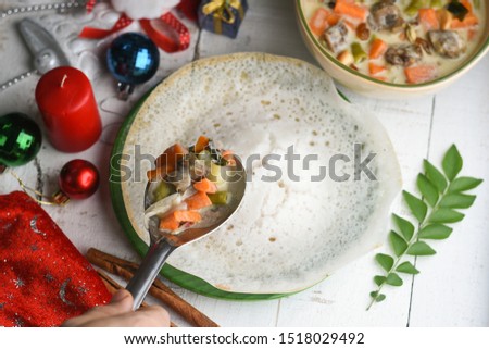 Indian Christmas celebration. Woman's hand serving Mutton stew on Appam, Kallappam a fermented rice pancake traditional christian Kerala breakfast for Christmas, New year, Easter in India.