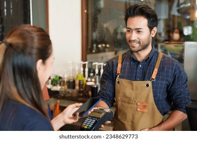 Indian coffee shop owner Submit an electronic cash register Have women use smartphone banking apps to pay for food and drink. Tap pay with credit card. No cash required. man smiling happily - Powered by Shutterstock