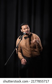 Indian Comedian Performing Stand Up Comedy And Telling Jokes In Microphone On Black