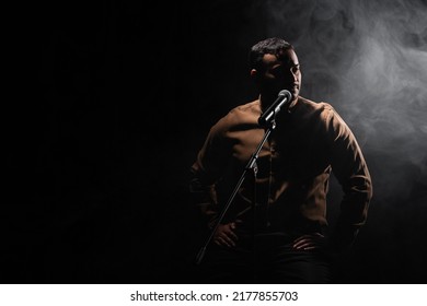 Indian Comedian Sitting On Chair And Performing Stand Up Comedy Into Microphone On Black With Smoke