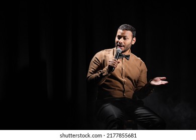 Indian Comedian Sitting And Performing Stand Up Comedy Into Microphone On Black