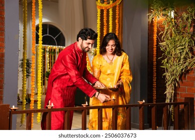 Indian couple celebrating Diwali by placing diyas on balcony, embracing tradition and family bonds - Powered by Shutterstock