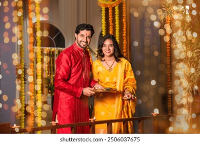 Indian couple celebrating Diwali by placing diyas on balcony, embracing tradition and family bonds - Powered by Shutterstock