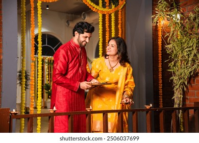 Indian couple celebrating Diwali by placing diyas on balcony, embracing tradition and family bonds - Powered by Shutterstock