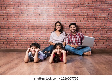 Indian Couple On Laptop While Kids Playing In Front Looking At Camera