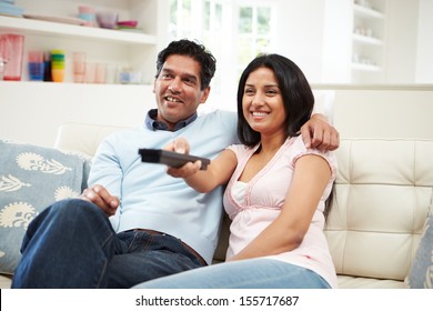 Indian Couple Sitting On Sofa Watching TV Together