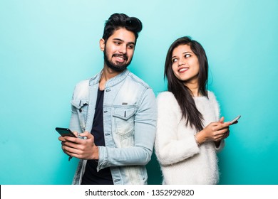 Indian Couple Standing Back To Back And Holding Mobile Phone Isolated On Green