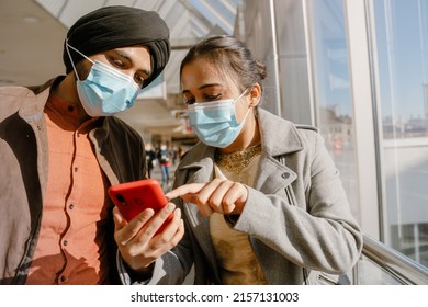 Indian Couple Wearing Face Masks Using Mobile Phone In Airport Indoors