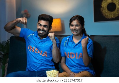 Indian couples celebrating indias win while watching live cricket sports match on tv or television at home - concept of Victory Celebration, Excited Fans and Emotional moment - Shutterstock ID 2355747017