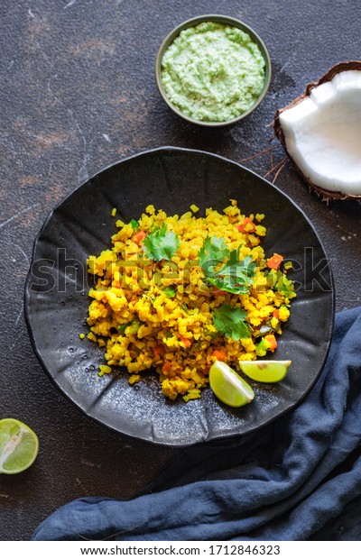 Indian\
cuisine. Poha or flattened rice typically Western Indian breakfast\
on black plate with coconut chutney sauce. national authentic\
vegetarian food. Asian travel food. top\
view